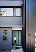 Dog and woman in front of grey metal façade of modern, cubist house in Brisbane, Australia