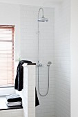 Shower with shower head and black towel draped over half-height partition wall