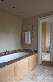 Badewanneneinbau mit Marmor Einfassung und geschnitzter Holzfront in renoviertem Bad