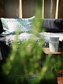 Blick durch Pflanzenzweige auf Sitzbank mit gemustertem Kissen