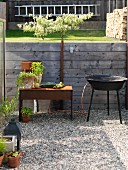 Potted herbs and harvested vegetables on rusty metal side table next to barbecue on gravel area in garden