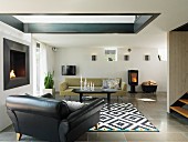 Schwarzer Ledersessel und Sofa um Couchtisch auf schwarz-weiss gemustertem Teppich im Wohnzimmmer mit Oberlichtfenster