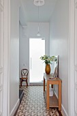 Hallway with tiled floor, console table and Thonet chair next to glass door
