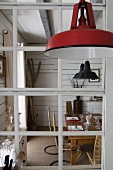Vintage pendant lamp with red lampshade in front of lattice interior window with view of dining table and designer chairs