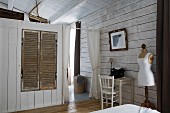 Fitted wardrobe with wooden louvre doors in partition, small desk against wall and vintage tailors' dummy in rustic bedroom