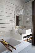 Modern bathtub next to masonry washstand in corner of bathroom with white wood-clad walls