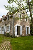 Rustikales Landhaus aus Naturstein mit weissen Fensterläden und Fenstern in sommerlichem Garten