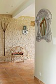 Mirror with carved frame, Scandinavian-style armchair and vintage pitchfork hung on stone wall