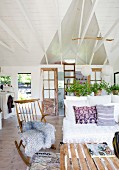 Sheepskin on rocking chair next to bench in open-plan interior with white-painted wood cladding