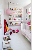 Child's bedroom with white cot, wall-mounted shelves and toys in wooden crates on castors