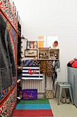 Narrow bedroom with striped rug, retro metal stool and wardrobe with ethnic patterns painted on front