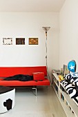Red designer sofa next to fitted, half-height shelves in contemporary interior