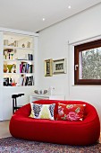 Red designer couch with patterned scatter cushions in corner of living room with white partition