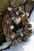 Pine cones stuffed with bird food decorating willow wreath propped up in snow