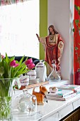 Vase of tulips, stacked books, tray of crockery and religious statue on shelf of serving hatch