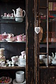 Floral crockery in wooden glass-fronted cabinet with peeling paint