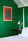 Abstract picture on wooden wall painted green next to bed with bedposts and snow-white bed linen