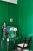 Dressing table with mirrored surfaces and antique chair against wooden walls painted a rich green