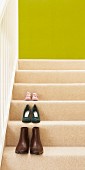 Pairs of shoes on treads of wooden staircase with cream stair carpet and spring green back wall