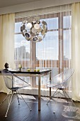 Clear, plexiglas shell chairs at modern dining table and Dandelion classic pendant lamp in front of glass wall with thread curtain