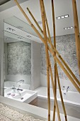Artistic bathroom with reflective mirrored surfaces; elephant-skin structure above bathtub and bamboo canes in foreground