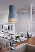 Pendant lamp with elegant fringed lampshade above dining table; sink unit with retro tap fittings in foreground
