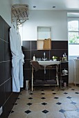 Bathroom with washstand against black-tiled wall and vintage-style towel rack with white dressing gowns hung on hooks