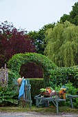 Vintage wheelbarrow decorated with harvested vegetables in front of trellis arch over garden gate and hedge
