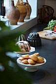 Madeleines and bundt cake on cake stands next to windowsill in country-house kitchen