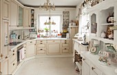 Fitted kitchen with cream fronts, jumble of ornaments on white dresser and utensils in colour-coordinated pastel shades