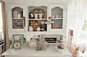 Antique kitchen scales and cake stands on white-painter dresser with crockery and knick-knacks in top section with chicken-wire door panels