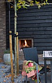 Dark wicker rattan chair and fire in outdoor fireplace on autumnal terrace