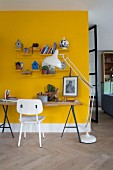 Tabletop on metal trestles against yellow wall, white-painted retro chair and modern standard lamp to one side