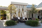 Trees in large planters and modern, dark wicker outdoor furniture on terrace in front of steel and glass façade