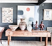 Exotic collection of vases and figurines on rustic wooden table below artworks on wall