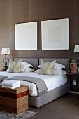 Graphic art above twin beds with grey upholstered frames, elegant scatter cushions and trunk at foot