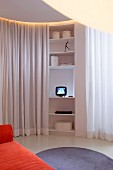 Tiny TV on curved shelves between white partition curtains and round, pale grey rug in front of orange sofa in living area