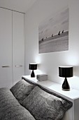 Grey patterned bed linen on bed, black table lamps on shelf and black and white photo of sailing boats