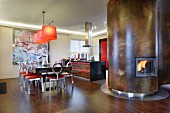 Dining area and open-plan kitchen in dark wood and stainless steel with red accents; curved, metal-clad partition with integrated fireplace