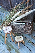 Rustic wooden stools next to wicker trunk and bunch of pampas grass on wooden deck