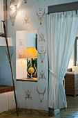 Table lamp in aperture in wall with ornate pattern stencilled on wall next to gathered white curtain in doorway