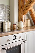 Kitchen counter with modern, retro-style cooker and embossed tiled splashback integrated into rustic roof-beam structure