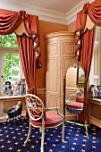 Corner of bedroom - chair with carved backrest painted antique white in front of cheval mirror on blue carpet with pattern of stars