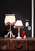 Lampshades decorated with pompoms, fringes and lace trim on country-house-style bases on top of antique steamer trunk