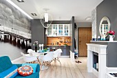 Dining area with Plastic Armchairs, blue sofa, black and white mural wallpaper and elegant fireplace with open-plan kitchen with partition walls in background