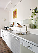 Modern kitchen counter with pale grey worksurface, kitchen utensils on shelf against wall