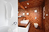 Mosaic wooden blocks covering walls, ceiling and floor in modern bathroom with washstand on base unit and wall-mounted toilet