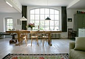 Langer Massivholztisch und schlichte Stühle vor Rundbogen Sprossenfenster in offenem Wohnraum mit ländlichem Flair
