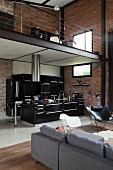 View past grey sofa and classic chair into black kitchen below gallery in loft apartment