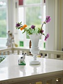 Garden flowers in white retro china vase and china cat on table
